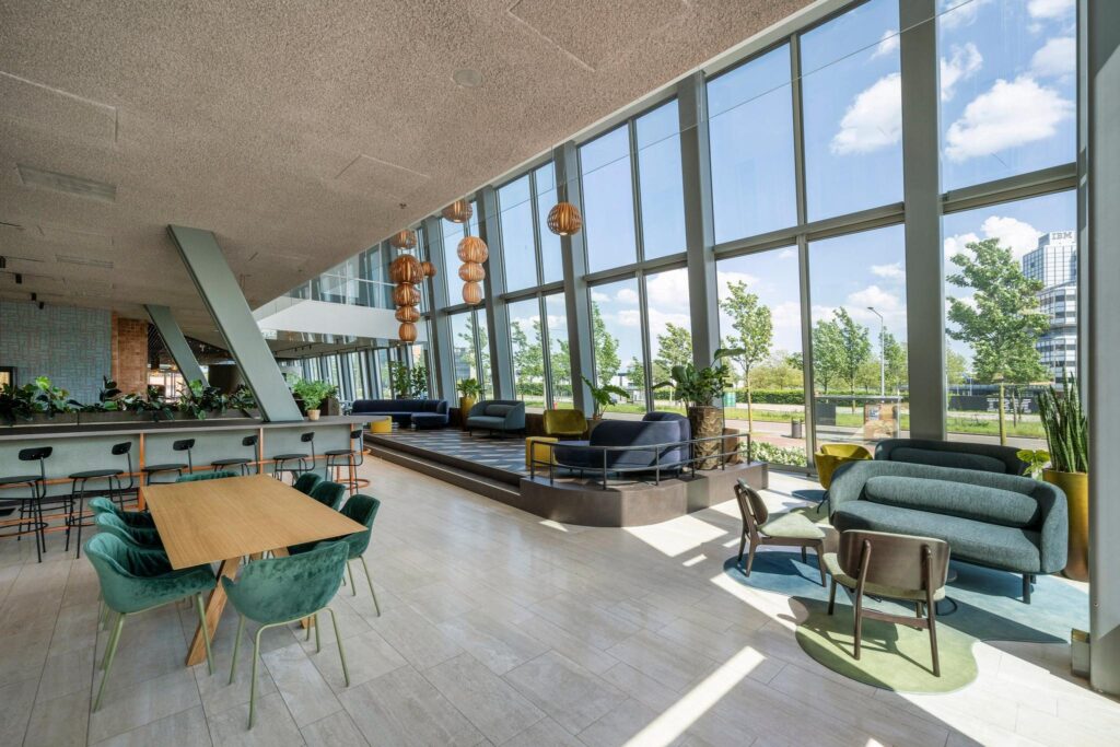 Moderne, lichtovergoten lobby aan de David Ricardostraat met designmeubilair en grote ramen die uitzicht bieden op een groene buitenomgeving.